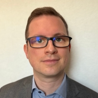 Markus Plischke, Mann mit kurzen braunen Haaren, Brille mit schwarzem Gestell, braunes Jacket und blaugraues Hemd.